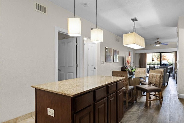 12527 Floridays Resort Dr Unit E-103, Orlando, FL 32821 - kitchen featuring a ceiling fan, dark brown cabinets, light stone countertops, a center island, and decorative light fixtures