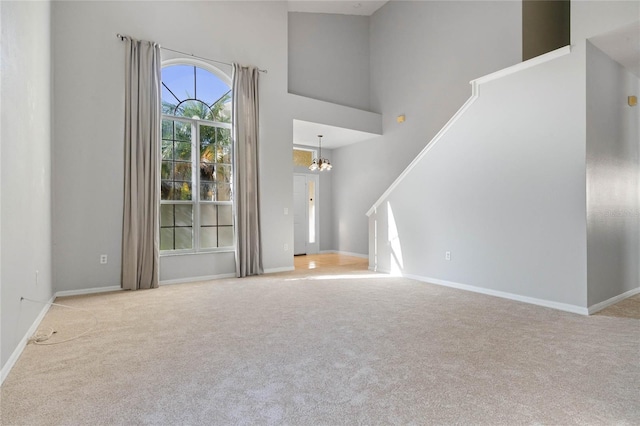 unfurnished living room with a notable chandelier, a towering ceiling, and light colored carpet