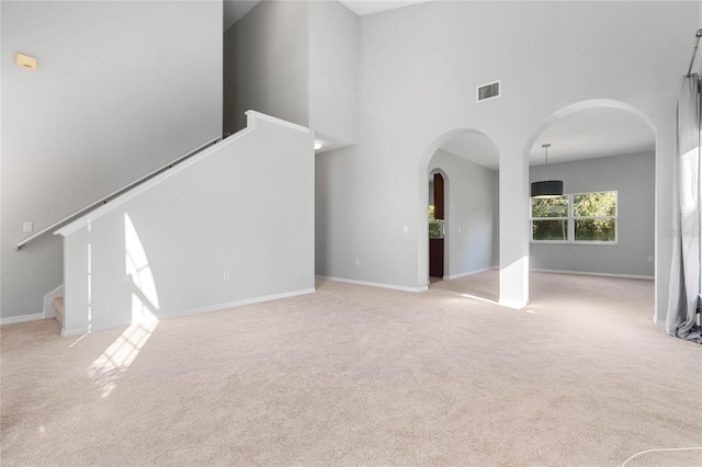 unfurnished living room featuring light carpet and a towering ceiling