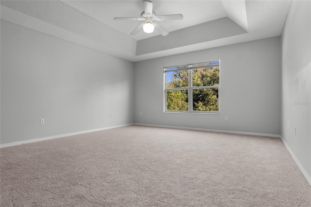 carpeted spare room featuring a textured ceiling, a tray ceiling, and ceiling fan