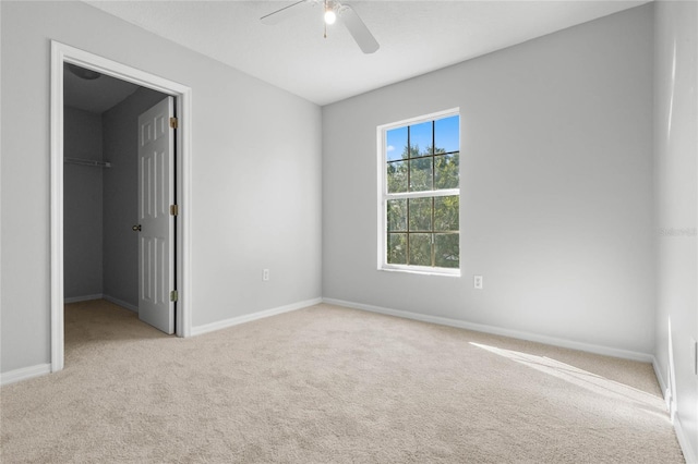 unfurnished bedroom featuring a spacious closet, light carpet, a closet, and ceiling fan