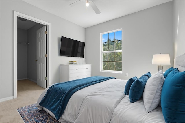 bedroom with a spacious closet, light colored carpet, a closet, and ceiling fan