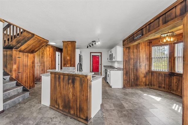 kitchen with white cabinetry, light stone countertops, kitchen peninsula, wooden walls, and appliances with stainless steel finishes