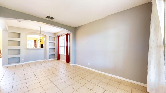 unfurnished living room featuring built in features, light tile patterned floors, and a notable chandelier