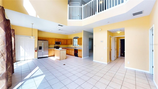 kitchen with a kitchen island, appliances with stainless steel finishes, decorative light fixtures, and a towering ceiling