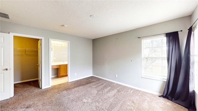 unfurnished bedroom featuring connected bathroom, a walk in closet, light colored carpet, a textured ceiling, and a closet