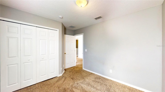 unfurnished bedroom featuring light colored carpet, a textured ceiling, and a closet