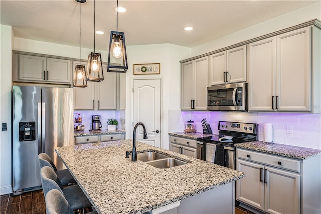 kitchen with sink, appliances with stainless steel finishes, a kitchen island with sink, and light stone counters