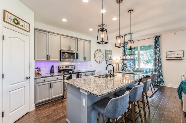 kitchen featuring appliances with stainless steel finishes, dark wood-type flooring, light stone countertops, and hanging light fixtures