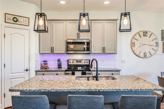 kitchen with decorative light fixtures, stainless steel appliances, a kitchen island with sink, and sink