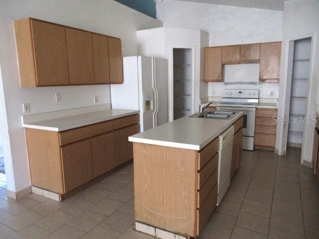 kitchen with light tile patterned floors, sink, a center island with sink, and white appliances