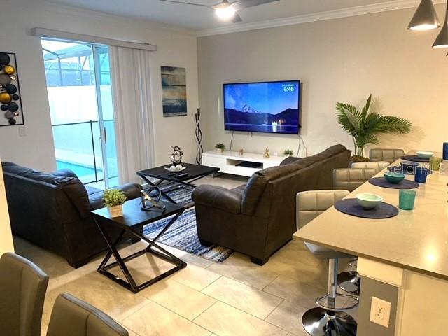 tiled living room with ornamental molding and ceiling fan