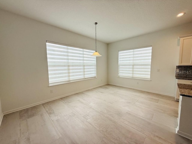 unfurnished dining area with a textured ceiling and baseboards