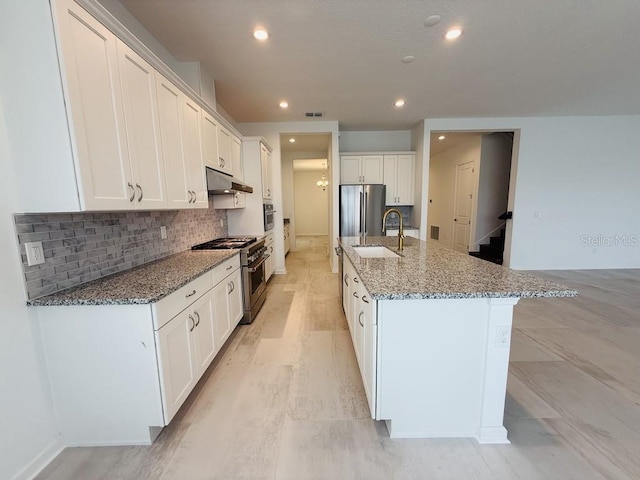 kitchen with under cabinet range hood, stainless steel appliances, a sink, white cabinets, and a center island with sink