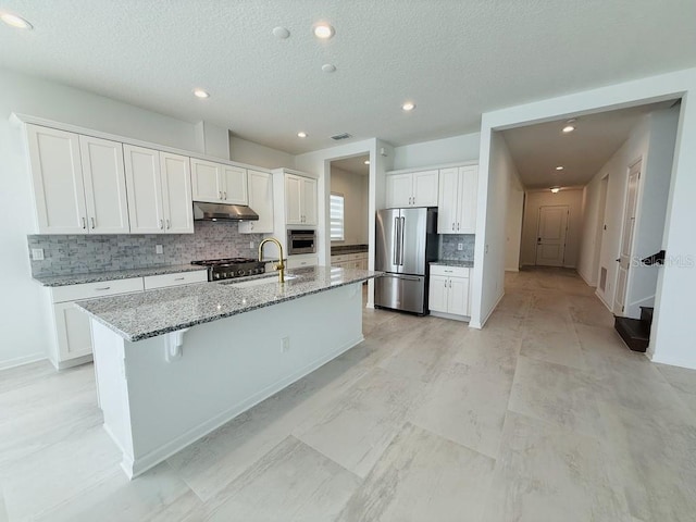 kitchen with light stone counters, stainless steel appliances, white cabinets, an island with sink, and under cabinet range hood