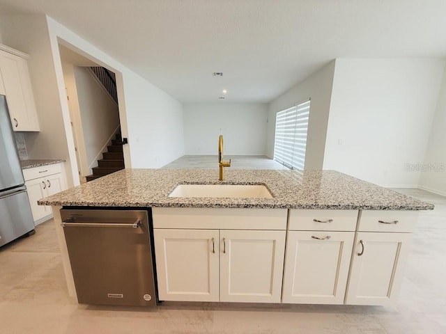 kitchen with white cabinets, an island with sink, freestanding refrigerator, light stone countertops, and a sink