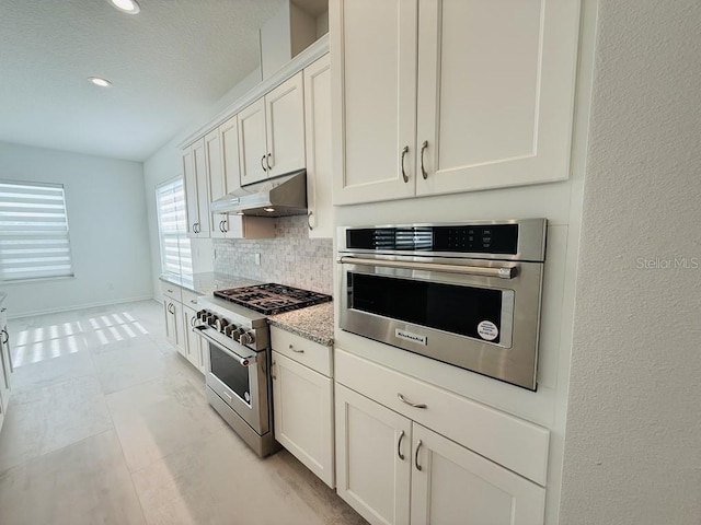 kitchen featuring light stone counters, under cabinet range hood, white cabinets, appliances with stainless steel finishes, and decorative backsplash