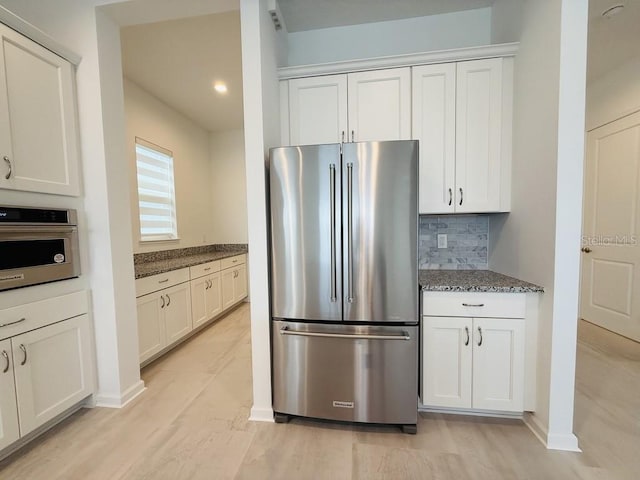 kitchen with decorative backsplash, appliances with stainless steel finishes, white cabinets, and dark stone countertops