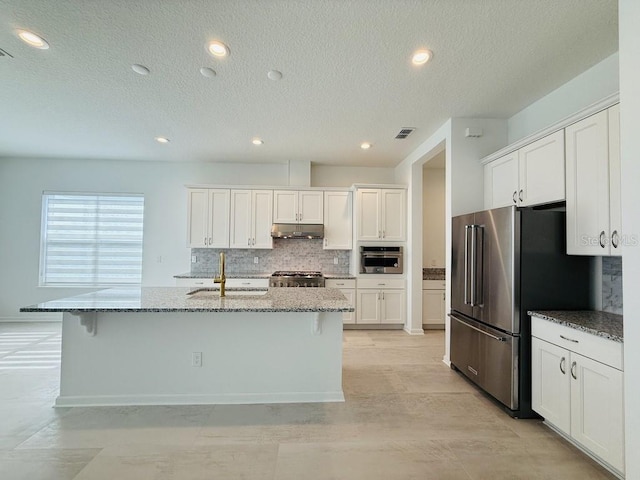 kitchen with stainless steel appliances, white cabinets, a center island with sink, and under cabinet range hood