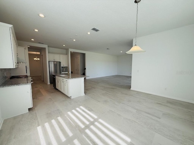 kitchen featuring visible vents, open floor plan, white cabinets, a sink, and an island with sink