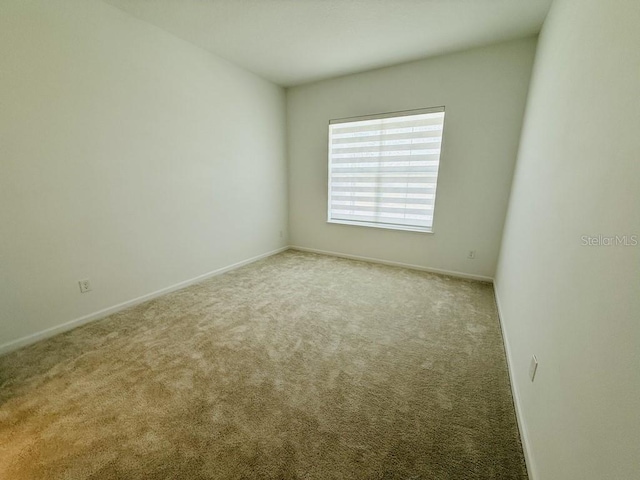 spare room featuring light carpet and baseboards