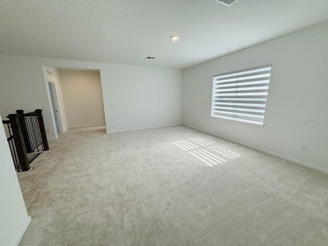 empty room featuring visible vents, baseboards, a textured ceiling, and light colored carpet