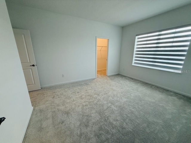 unfurnished bedroom with baseboards, a spacious closet, and light colored carpet