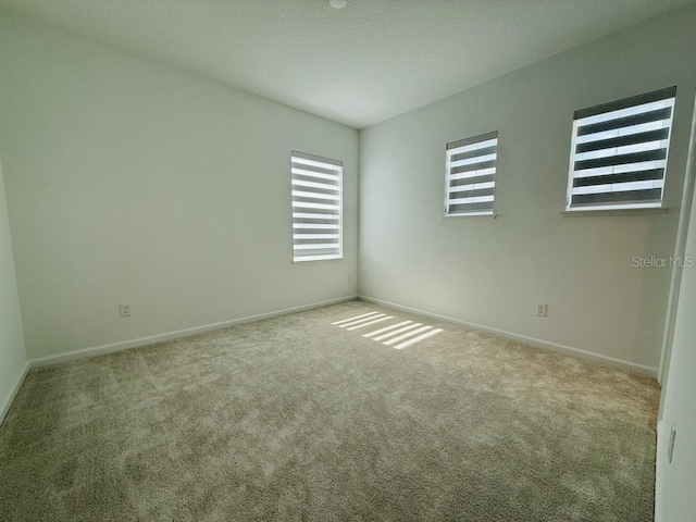 empty room featuring light colored carpet, a textured ceiling, and baseboards