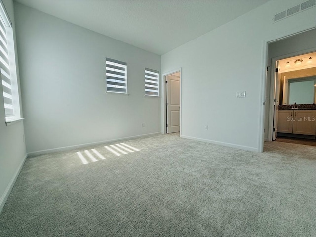 unfurnished bedroom featuring baseboards, a sink, visible vents, and light colored carpet