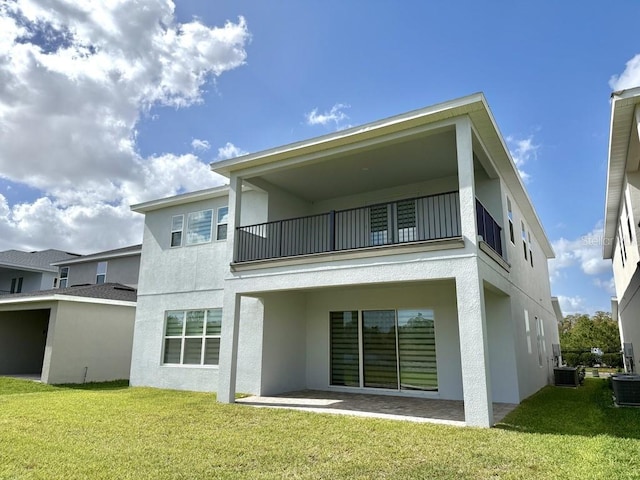 rear view of house featuring a yard, central AC, a balcony, and stucco siding