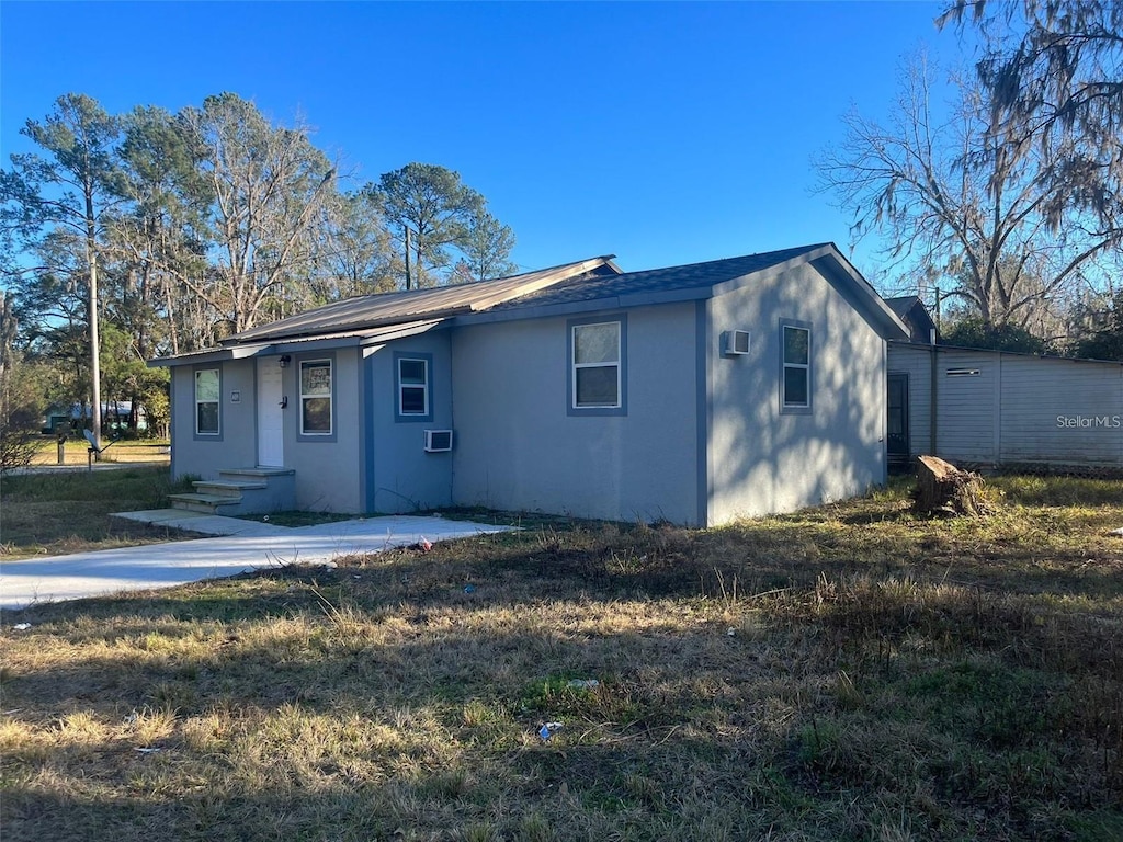 view of front of house with a wall unit AC and a front lawn