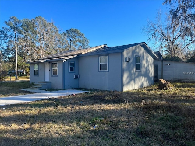 view of front of house with a wall unit AC and a front lawn