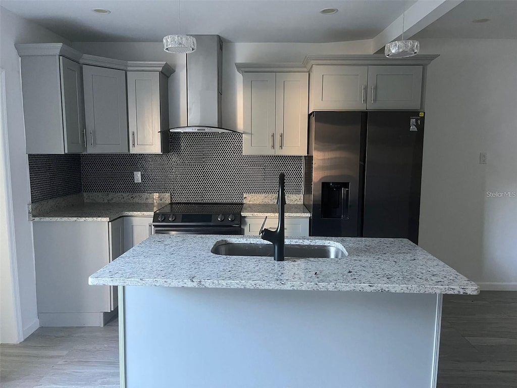 kitchen with wall chimney range hood, a center island with sink, sink, black appliances, and light stone counters