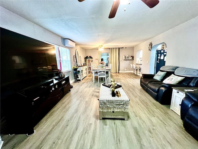 living room with a textured ceiling, an AC wall unit, light wood-type flooring, and ceiling fan