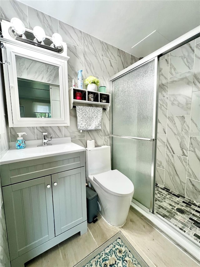 bathroom with a shower with door, vanity, toilet, and tile walls