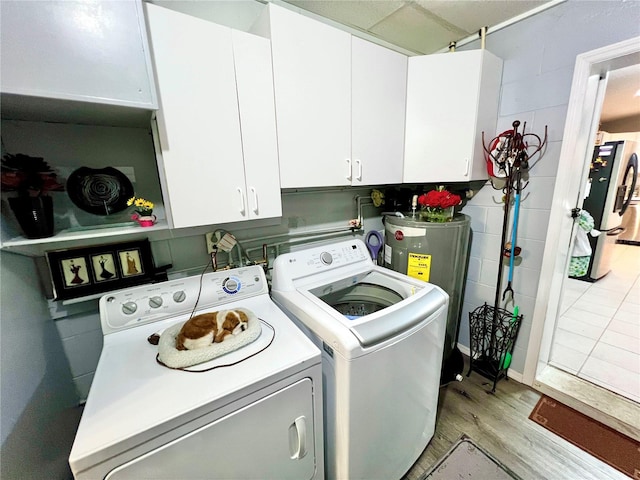 washroom with light hardwood / wood-style flooring, electric water heater, separate washer and dryer, and cabinets