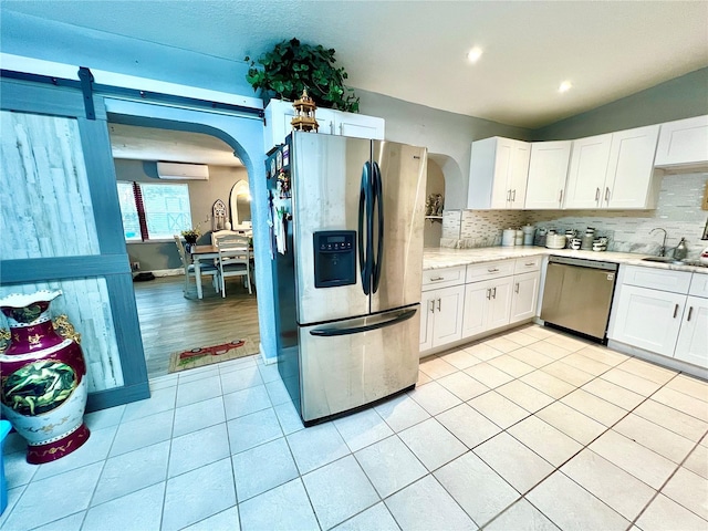 kitchen featuring appliances with stainless steel finishes, lofted ceiling, a wall unit AC, and white cabinets