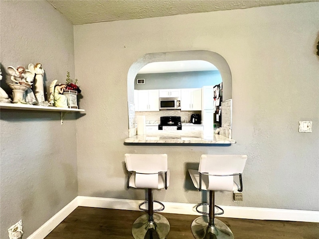 interior space with decorative backsplash, white cabinets, dark wood-type flooring, and black range