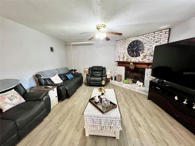 living room featuring light hardwood / wood-style flooring, a fireplace, a textured ceiling, and ceiling fan