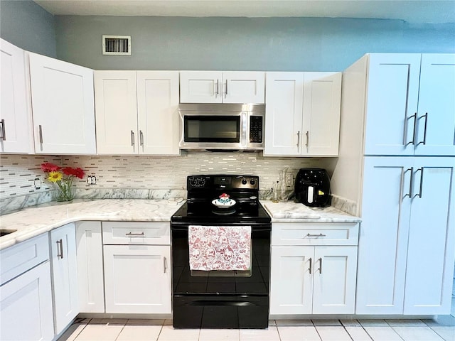 kitchen with black / electric stove, light stone countertops, white cabinetry, and light tile patterned flooring