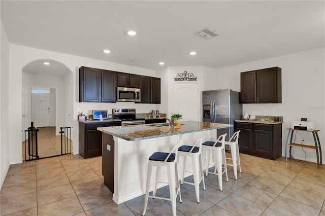 kitchen featuring dark brown cabinets, a center island with sink, a kitchen bar, stainless steel appliances, and sink