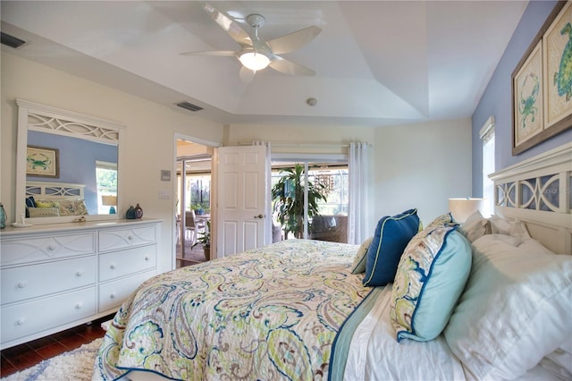 bedroom featuring ceiling fan, a tray ceiling, multiple windows, and dark hardwood / wood-style floors