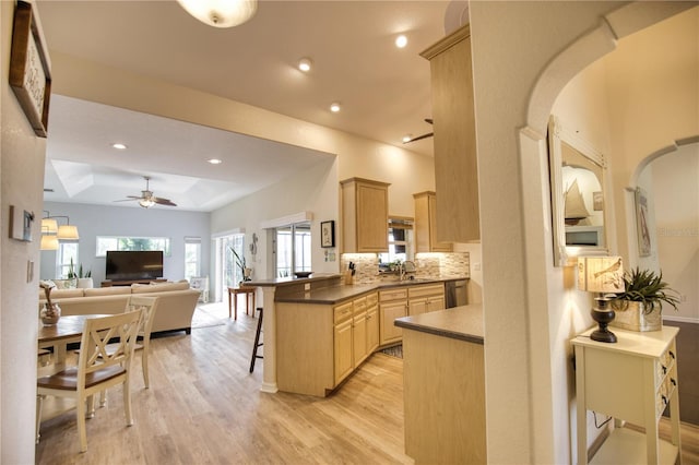 kitchen featuring kitchen peninsula, a kitchen breakfast bar, a tray ceiling, light brown cabinetry, and light wood-type flooring