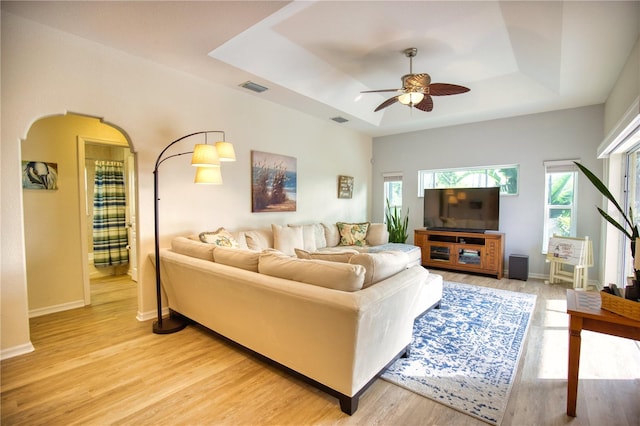 living room with ceiling fan, a raised ceiling, and light wood-type flooring