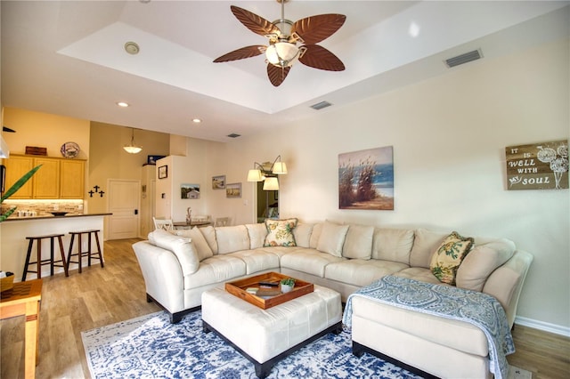 living room with light hardwood / wood-style floors, a raised ceiling, and ceiling fan