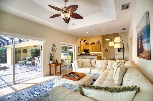 living room with ceiling fan, a raised ceiling, and light hardwood / wood-style flooring