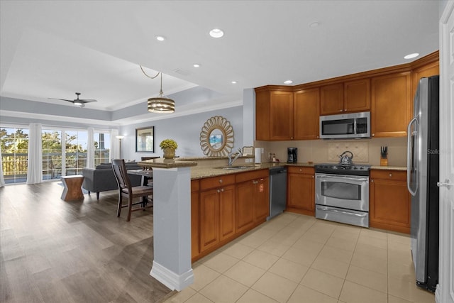 kitchen featuring ceiling fan with notable chandelier, light stone countertops, appliances with stainless steel finishes, a tray ceiling, and kitchen peninsula