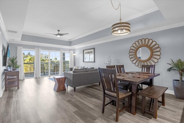 dining space with a raised ceiling, hardwood / wood-style floors, and ceiling fan with notable chandelier