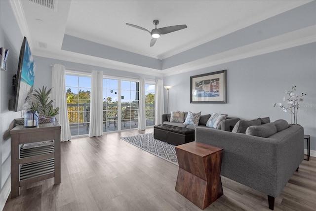 living room with hardwood / wood-style floors, a raised ceiling, ceiling fan, and ornamental molding