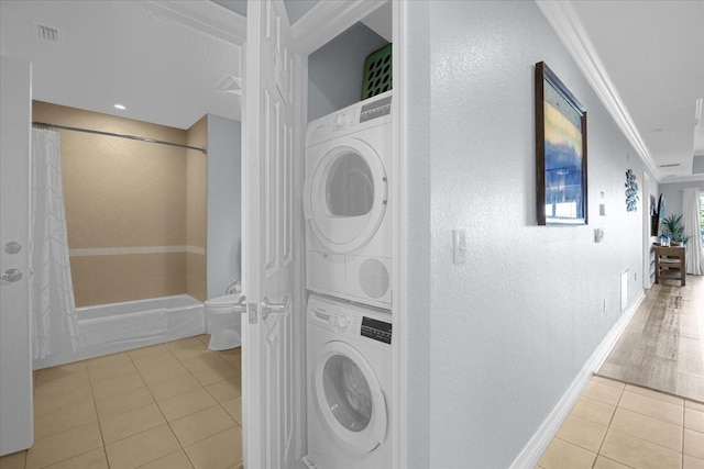 clothes washing area featuring crown molding, light tile patterned flooring, and stacked washing maching and dryer